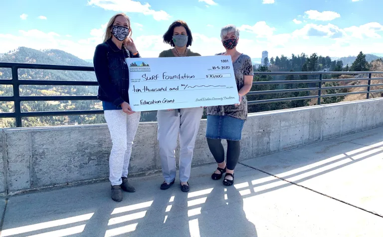 Three people stand on a sidewalk with a giant check 