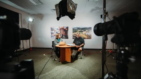 2 people sitting at table speaking on-camera