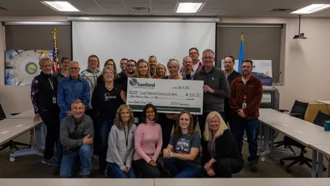 large group of surf employees present a giant check for breast cancer awareness
