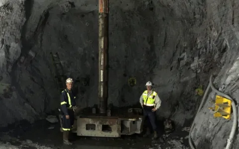 2 workers stand underground with equipment