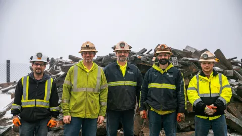 group of men smiling in front of pile of rubble