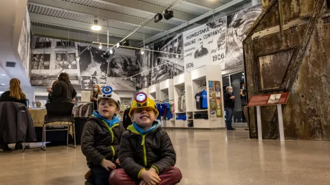 2 young boys smile while wearing novelty mining hats in the visitor center.