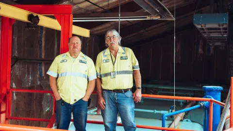 2 waste water treatment employees standing in front of the tanks