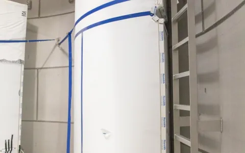 The outside of the LZ water tank. A tall white cylinder  with blue tape inside a large stainless steel looking tank. 