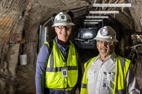 Mike Headley (left) the executive director of the SDSTA and the laboratory director at SURF stands next to Casey Peterson, SDSTA board chair, just before Peterson touched off the first blast in the excavation of SURF’s expansion located 4850 feet below the surface.  Both are wearing full PPE required underground inclding reflective vest, hard hat, and light.