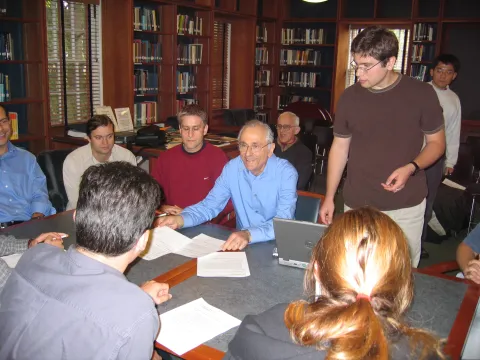 John Bahcall surrounded by students at a desk 