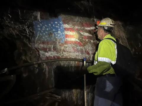 Kyle Ehnes  looks at a flag underground painted onto a rock wall, his head lamp illumnites the colors on the rock
