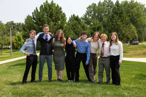 The 2024 Davis-Bahcall Scholars include: (L-R) Colby Routh, Beck Bruch, Nicolette Dame, Huixin Zhang, James Roth, Mackenzie Hollenbeck, Jing Yan, and Ashley Tieszen - standing on green grass outside dressed up for their presentations.