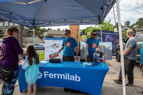 The tent for Fermilab at Neutrino Day was a popular place for many.  Participants are gathered around the fermilab tent.