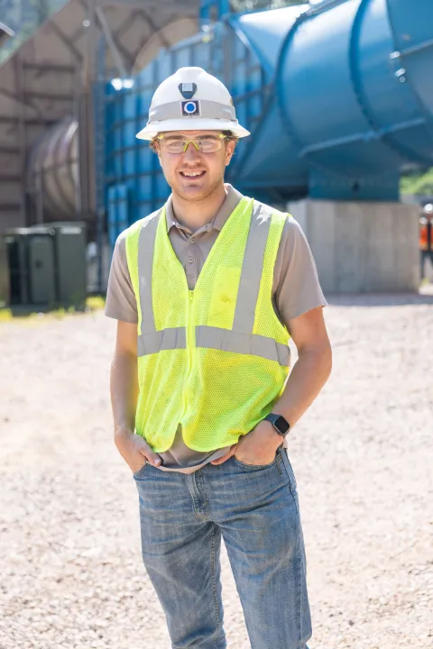 Bridger Roberdeau, a 2024 engineering intern at SURF, stands in front of the blew Oro Hondo Fan in PPE including a hard hat, safety glasses, and a reflective vest.
