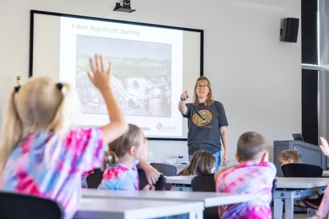 Children in a classroom at SURF raise their hands to engage with a science education specialist