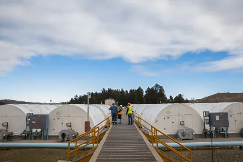 3 people on a metal foot bridge running between rows of semi-circular structures