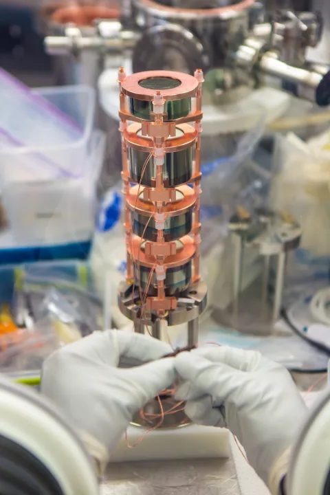 A researcher wearing gloves assembles a germanium detector inside a glovebox, carefully handling thin wires in a clean lab environment