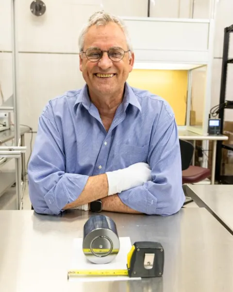 ORNL’s David Radford sits in a lab, smiling beside his germanium detector, with its central contact visible at the 3-inch mark.