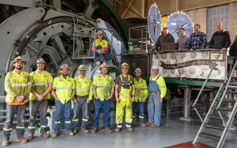 13 people standing in front of large hoisting equipment