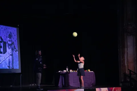 A child bounces a ball on stage.