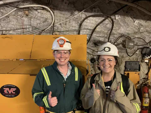 Schleich and Bowers pose here together on the 4850 Level of SURF in front of a large piece of equipment.  They are both wearing full PPE needed in the underground. 