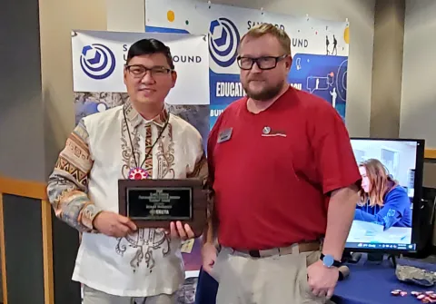 Ronald Brillantes of Pahin Sinte Owayawa School in the Porcupine School District holding his award with Chad Ronish of SURF at the booth for SURF at the 2026 STEM Ed Conference