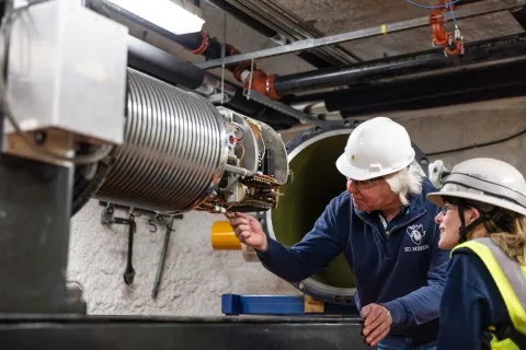 A photo of two poeple looking inside an open component of the CASPAR experiment 