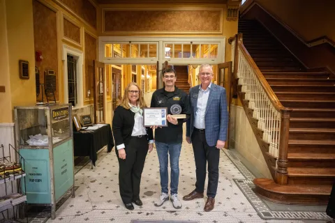 Mike Headley, Todd Jones, and Ann Metli stand in the hallway of the Homestake Opera House with the 2025 CORES Award. 