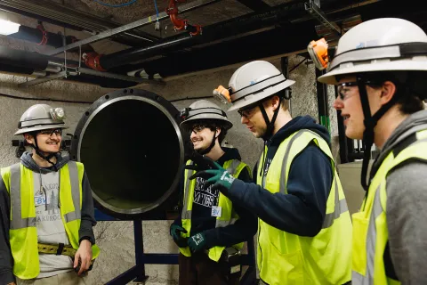 Students converse next to a component for the CASPAR experiment 