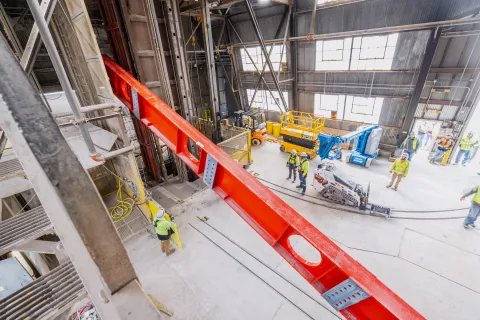 Technicians rig DUNE cryostat beams for loading into the cage--the lift has begun. 