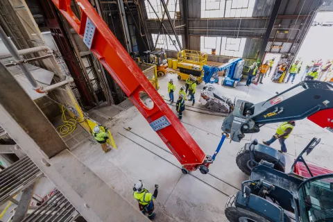 Technicians rig DUNE cryostat beams for loading into the cage - the beam is halfway in. 