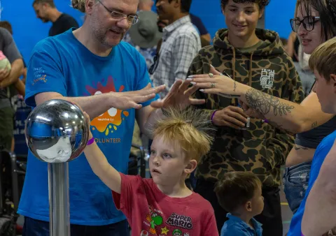 A child holds onto an Van der Graaf Generator making his hair stand on end