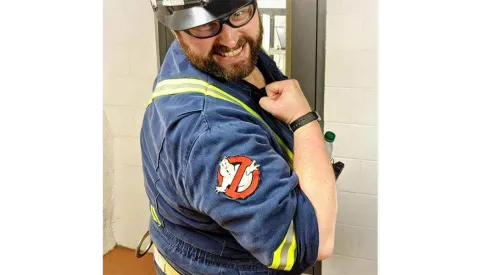 Person in hardhat, safety glasses, and underground safety wear flexes to show off "Ghost Busters" patch on their arm