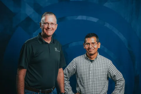Two people stand in front of a dark blue backdrop
