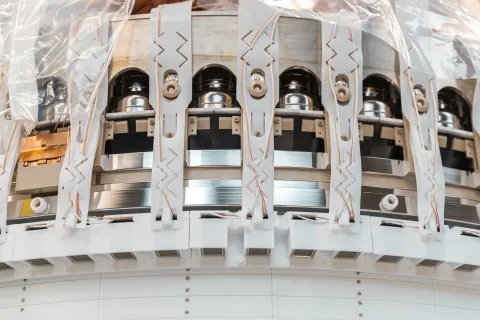 A close-up of the top of the recently assembled LUX-ZEPLIN xenon detector in the Surface Assembly Lab cleanroom at Sanford Underground Research Facility on July 26, 2019. White PTFE reflective paneling lines much of the detector. From the outside, a viewer can see the stainless-steel outer rings of the electric grids, the back of the PMT array and some of the PMT cabling. Photo by Nick Hubbard, Sanford Underground Research Facility.