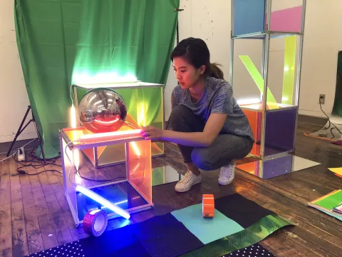 An artist kneels amidst an exhibit in-progress