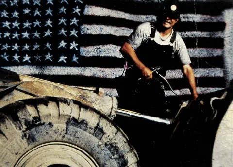 An employee services underground equipment in front of Hover's painting of an American flag on the 7400 Level of the former Homestake Gold Mine.