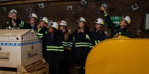 students in underground personal protective equipment stand in a drift and point into the air