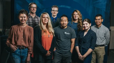 Eight people smile at the camera in front of a blue backdrop