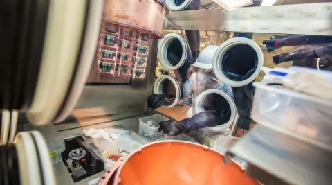 Researcher in cleanroom garb works in glovebox containing a Majorana cryostat. 