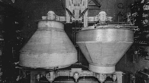 "The Nordberg Manufacturer’s double drum hoist is shown from above. The diameter at one end is 25 feet and tapers to a diameter of 12 feet at the other end, allowing them to sit opposite each other and shrink the footprint of the drums. Courtesy Siemag Tecberg, Inc." image "black and white photo of…ists aligned from above"