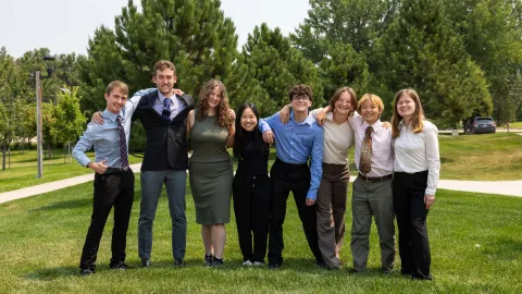 The 2024 Davis-Bahcall Scholars include: (L-R) Colby Routh, Beck Bruch, Nicolette Dame, Huixin Zhang, James Roth, Mackenzie Hollenbeck, Jing Yan, and  Ashley Tieszen - standing on green grass outside dressed up for their presentations.  