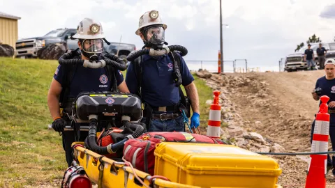 Students wearing PPE and breathing units while moving a cart full of gear at the 2024 Mine Rescue Competition at SURF 