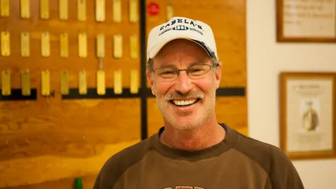 Kip Johnson wearing a baseball cap and a brown shirt in front of a brass tag board at SURF. 