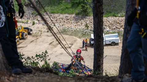 A person on a steep slope in full PPE tied into a set of ropes helping hoist up a stretcher during rescue training at SURF.
