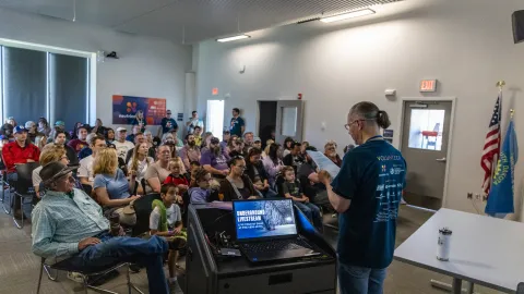 A crowd sits in a room with a speaker wearing a ND shirt