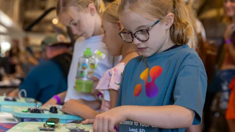 Children engaged in hands on learning activities with circut boards provided by the 2025 SURF artist in Residence Chris Combs at Neutrino Day in Lead, SD.